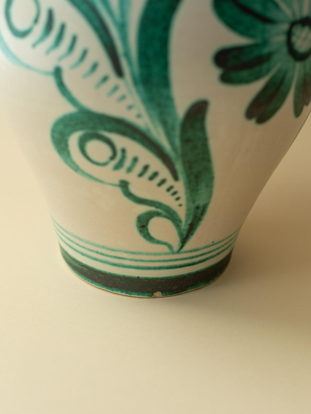 A cream coloured vintage ceramic vase by Kupittaan Savi with a handpainted floral motif in green. Scandinavian design from Finland. A view of lower part of the vase.