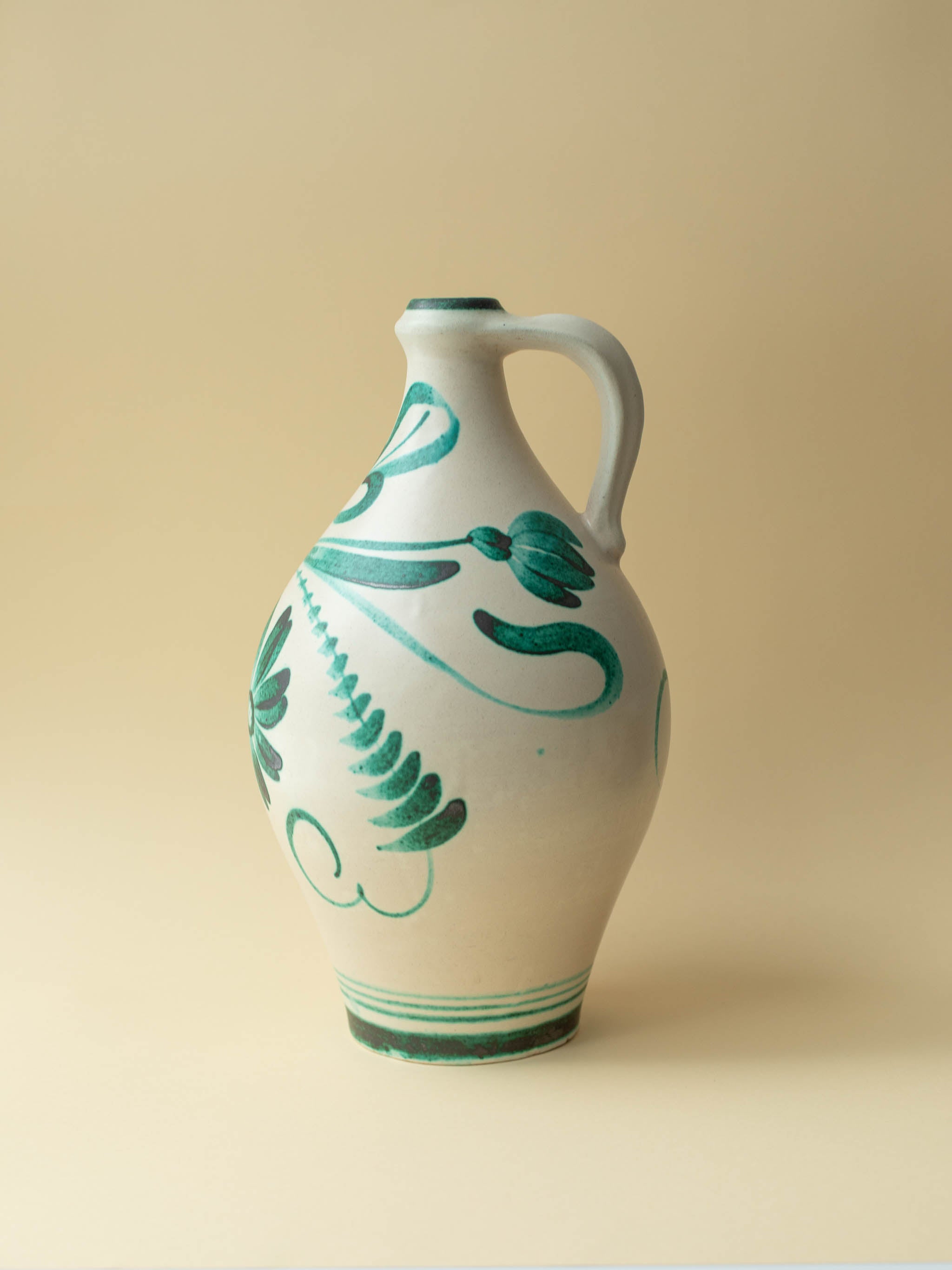 A cream coloured vintage ceramic vase by Kupittaan Savi with a handpainted floral motif in green. Scandinavian design from Finland. A view of the back left side.