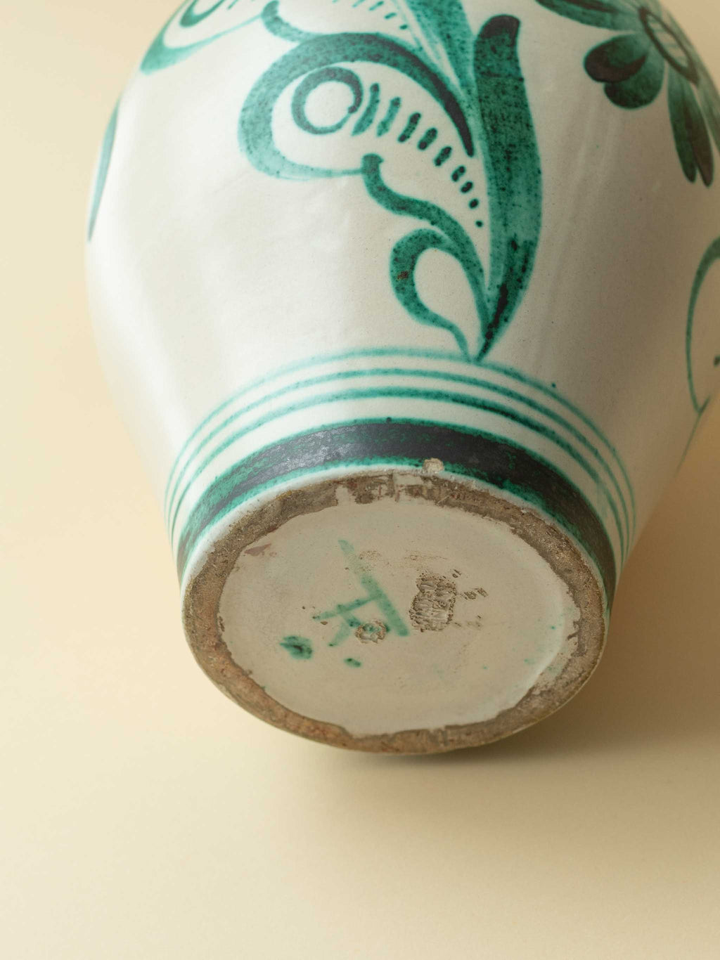 A cream coloured vintage ceramic vase by Kupittaan Savi with a handpainted floral motif in green. Scandinavian design from Finland. A view of the bottom showing the signature. Signed TK for Tapio Kinnunen.