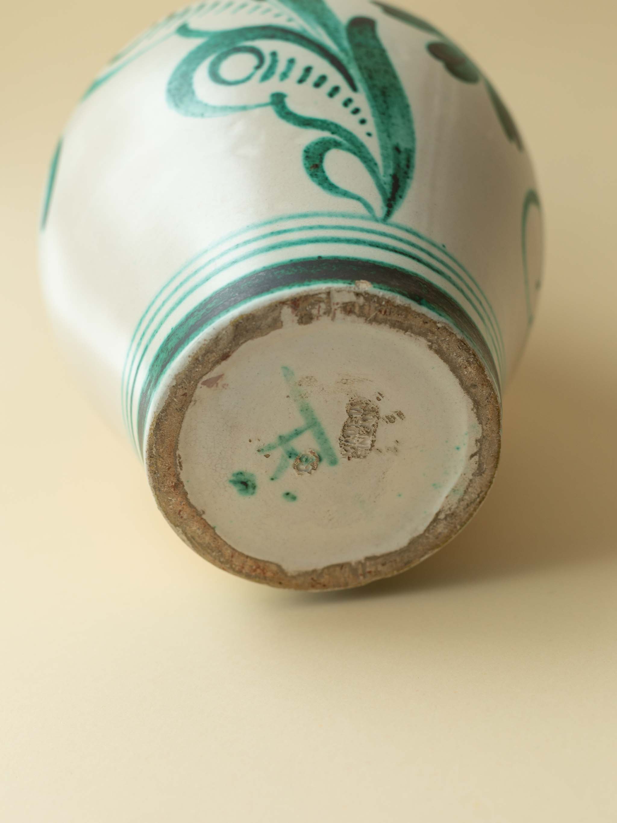 A cream coloured vintage ceramic vase by Kupittaan Savi with a handpainted floral motif in green. Scandinavian design from Finland. A straight view of the bottom, showing the signature.