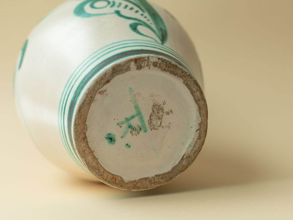 A cream coloured vintage ceramic vase by Kupittaan Savi with a hand painted floral motif in green by Tapio Kinnunen. Scandinavian design from Finland. A close up view of the bottom, showing the signature TK for Tapio Kinnunen.