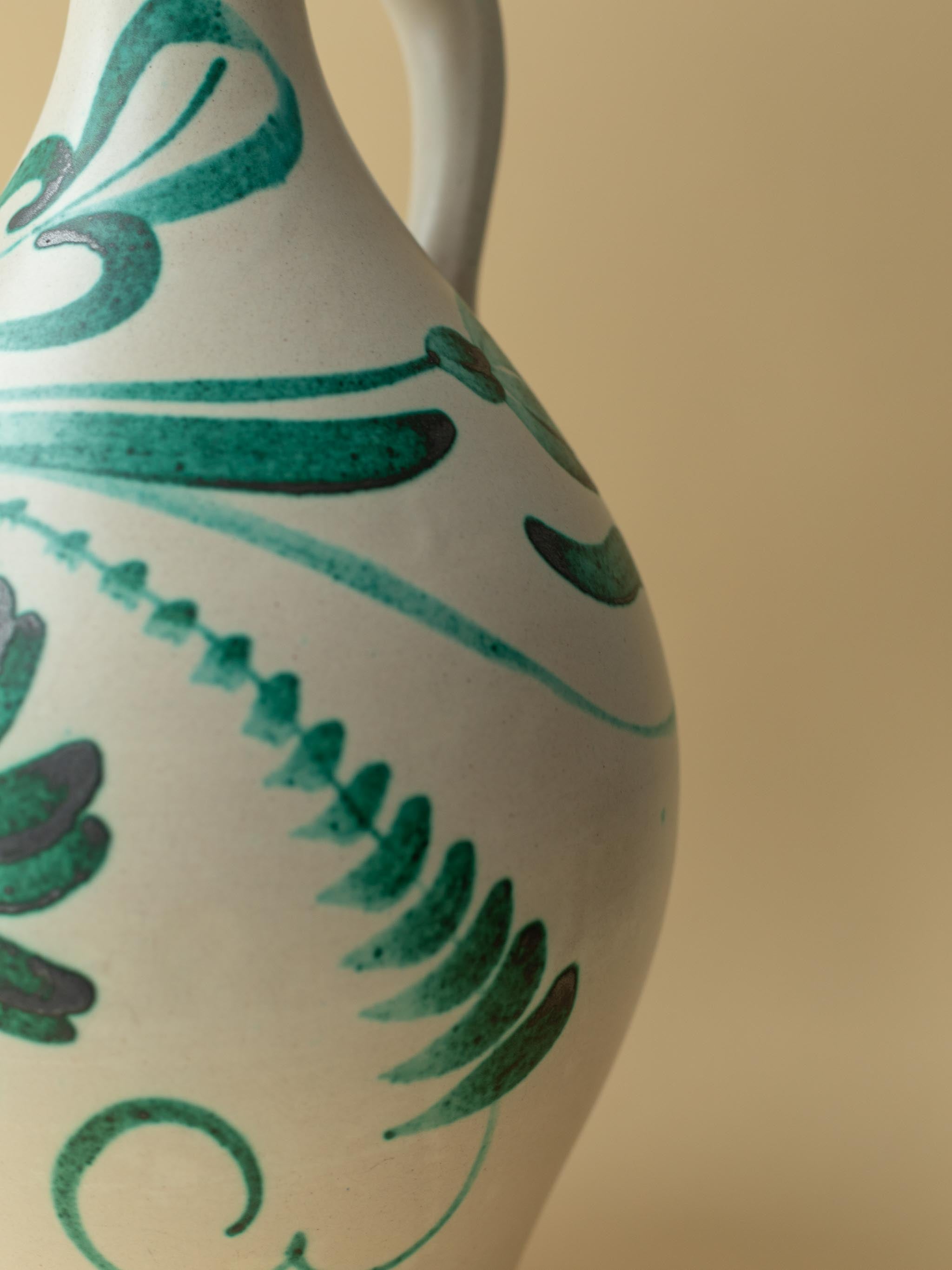 A crean coloured vintage ceramic vase by Kupittaan Savi with a handpainted floral motif in green. Scandinavian design from Finland. A close up view from the side.