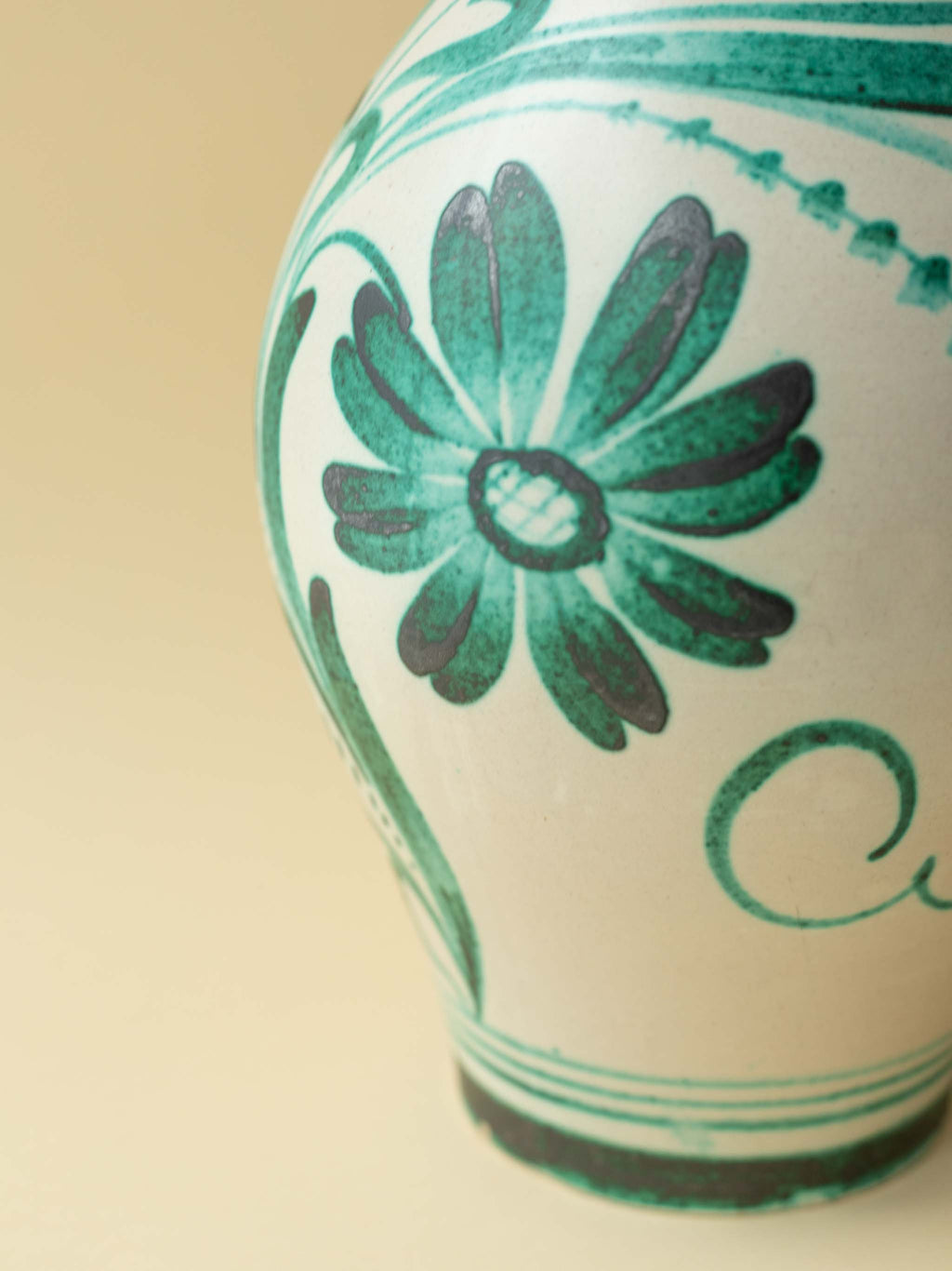 A crean coloured vintage ceramic vase by Kupittaan Savi with a handpainted floral motif in green. Scandinavian design from Finland. A close up view of the flower motif.