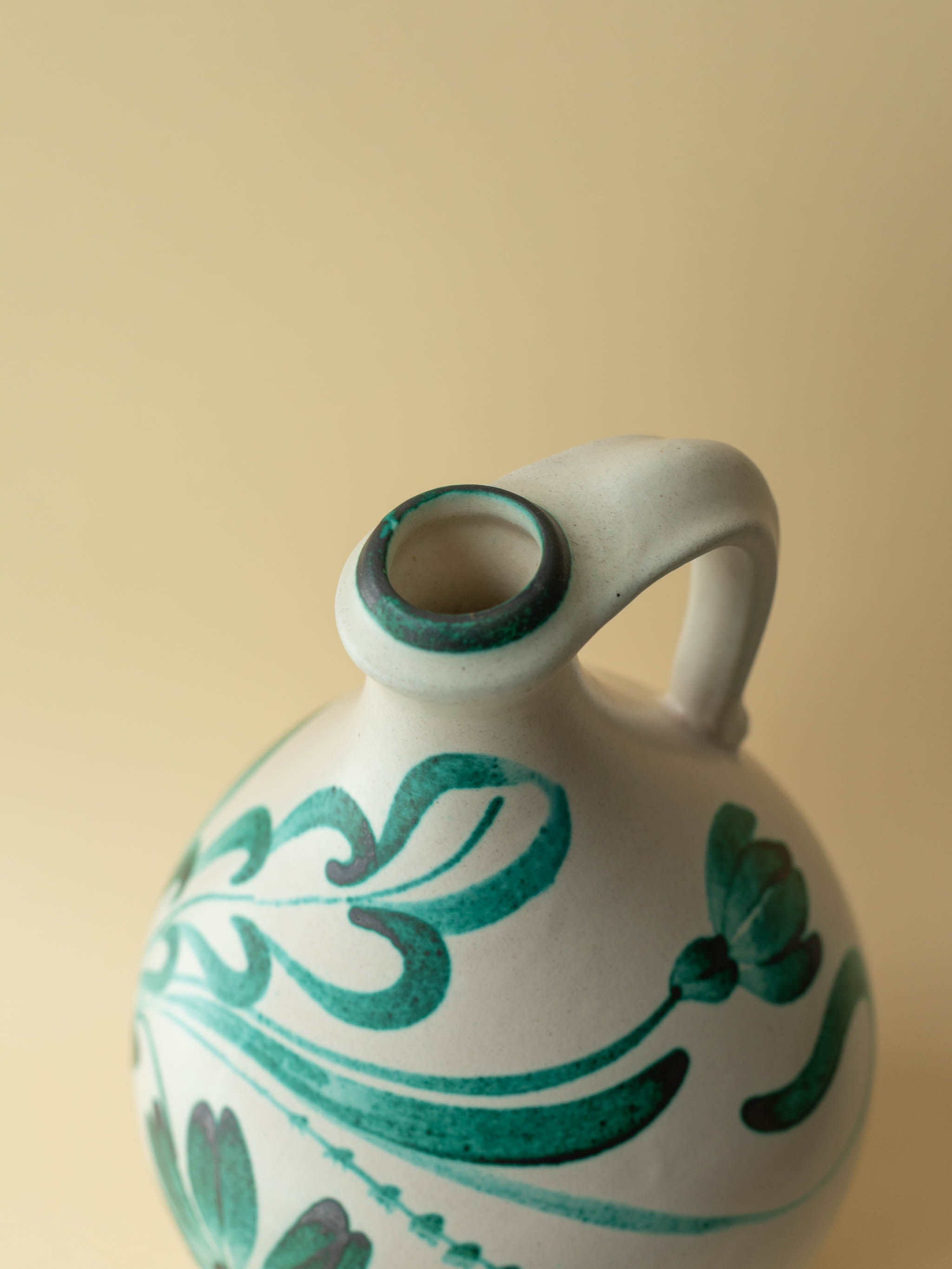 A cream coloured vintage ceramic vase by Kupittaan Savi with a handpainted floral motif in green. Scandinavian design from Finland. A view from above, front.