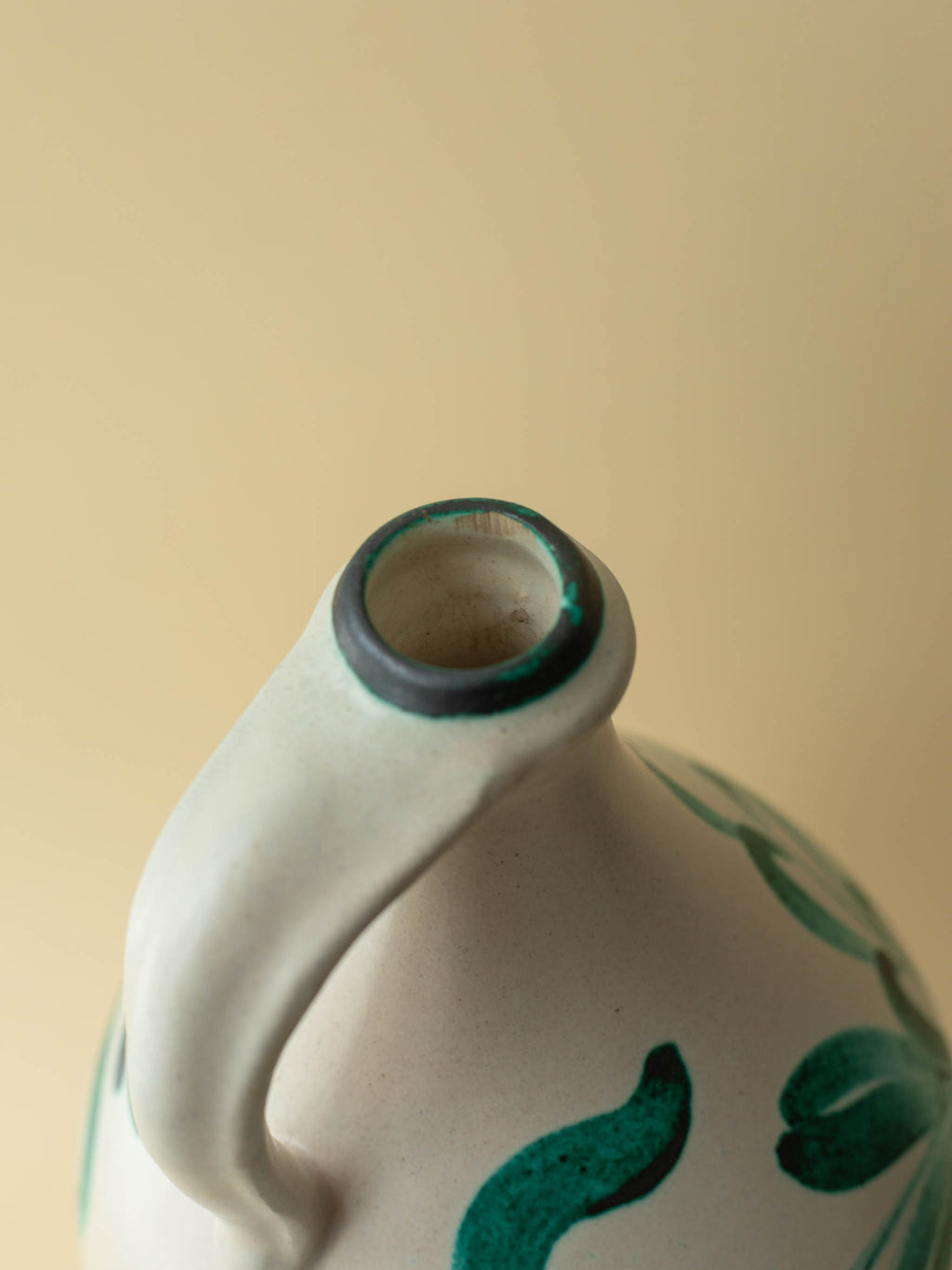A cream coloured vintage ceramic vase by Kupittaan Savi with a handpainted floral motif in green. Scandinavian design from Finland. A view of the top.