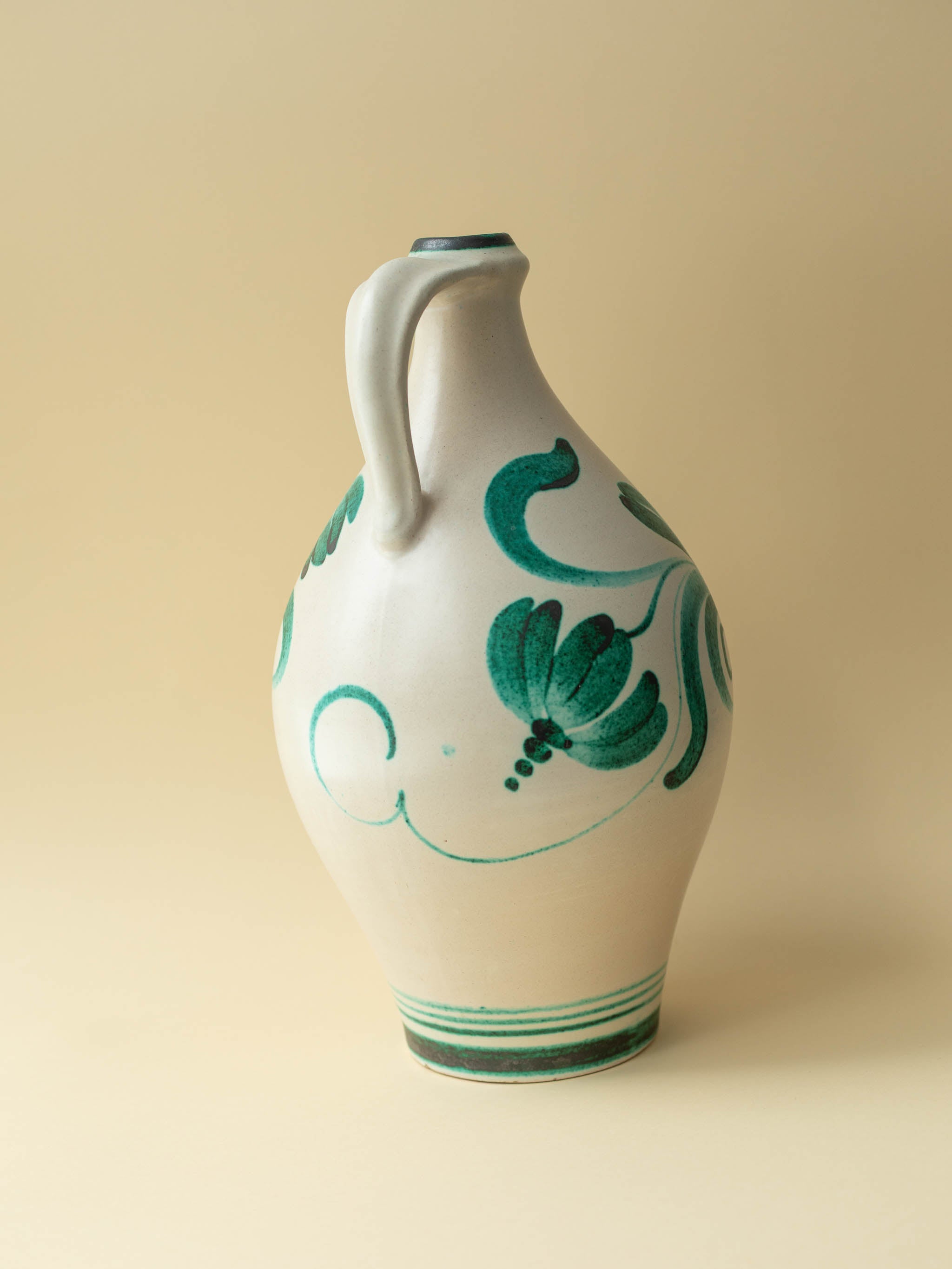 A cream coloured vintage ceramic vase by Kupittaan Savi with a handpainted floral motif in green. Scandinavian design from Finland. A view of the back side.