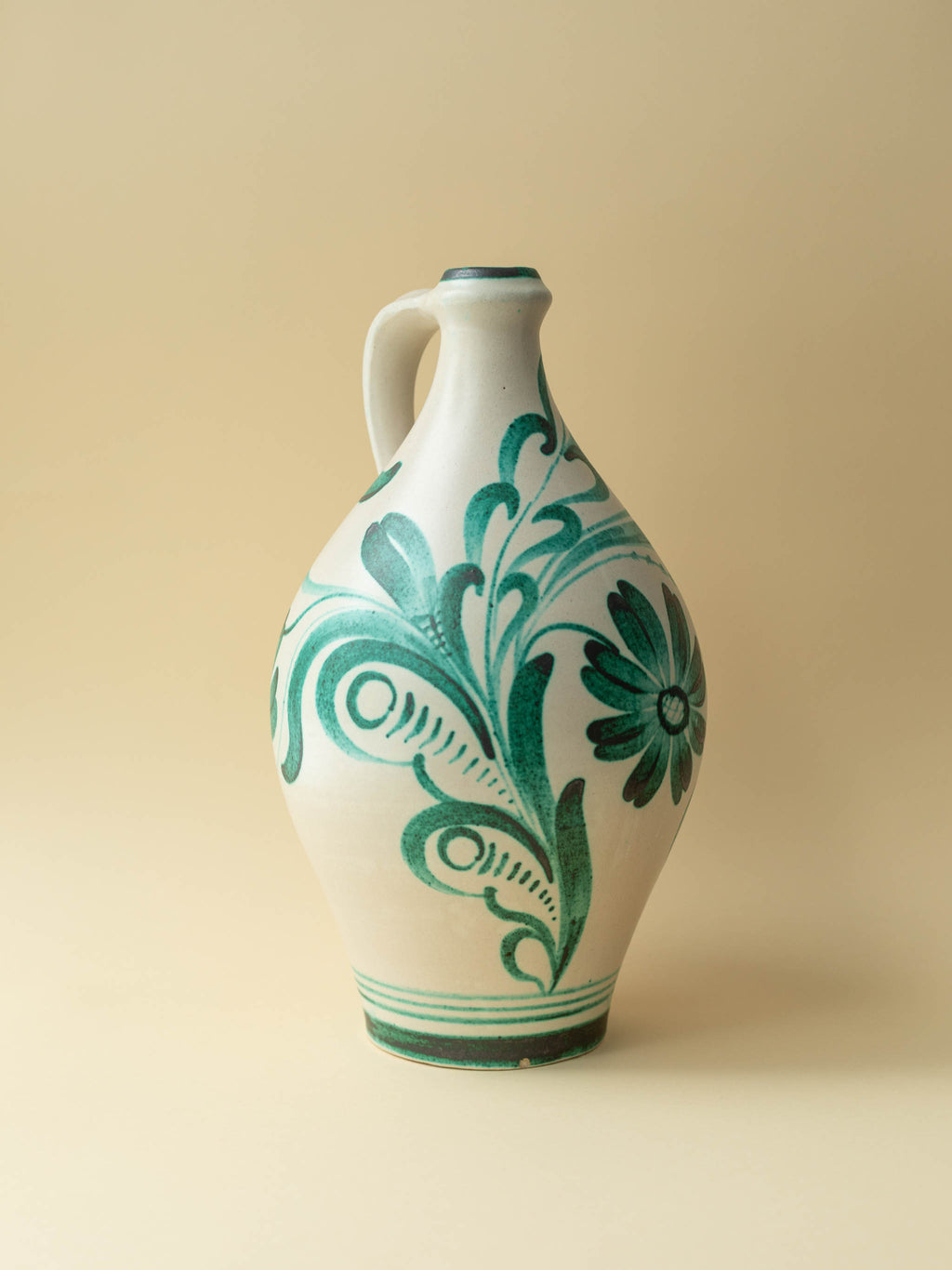 A cream coloured vintage ceramic vase by Kupittaan Savi with a handpainted floral motif in green. Scandinavian design from Finland. A view of the front right side.