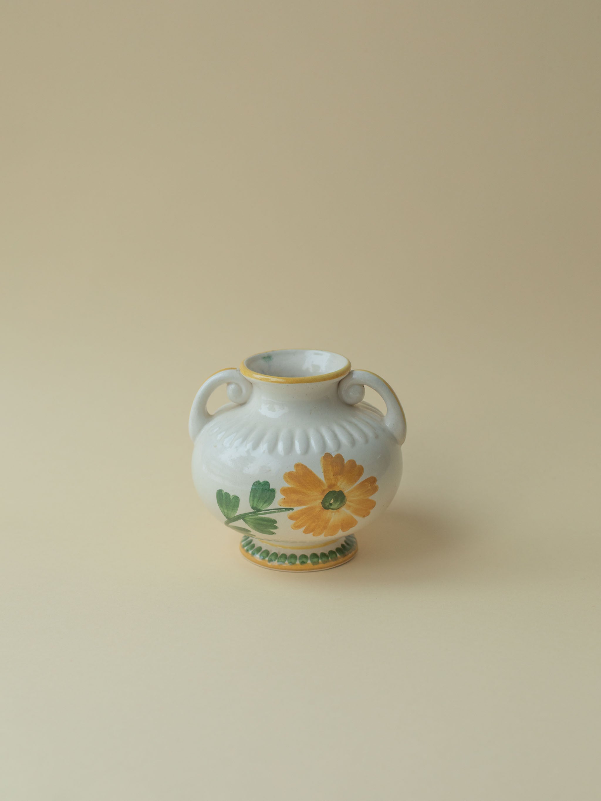 A white vintage ceramic vase by Kupittaan Savi with a handpainted floral motif in green and yellow. Scandinavian design from Finland. A view from the front.