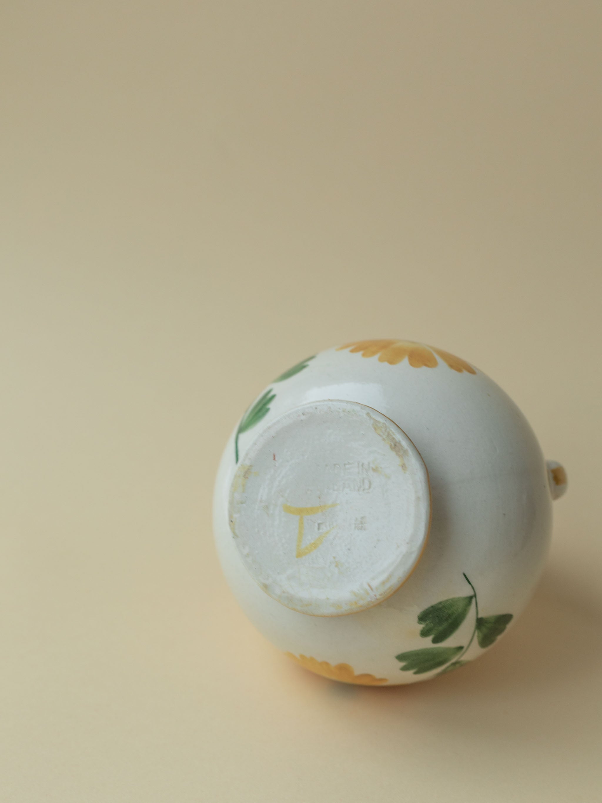 A white vintage two handled ceramic vase by Kupittaan Savi with a handpainted floral motif in green and yellow. Scandinavian design from Finland. A view of the bottom, showing the stamp and numbering or signature.