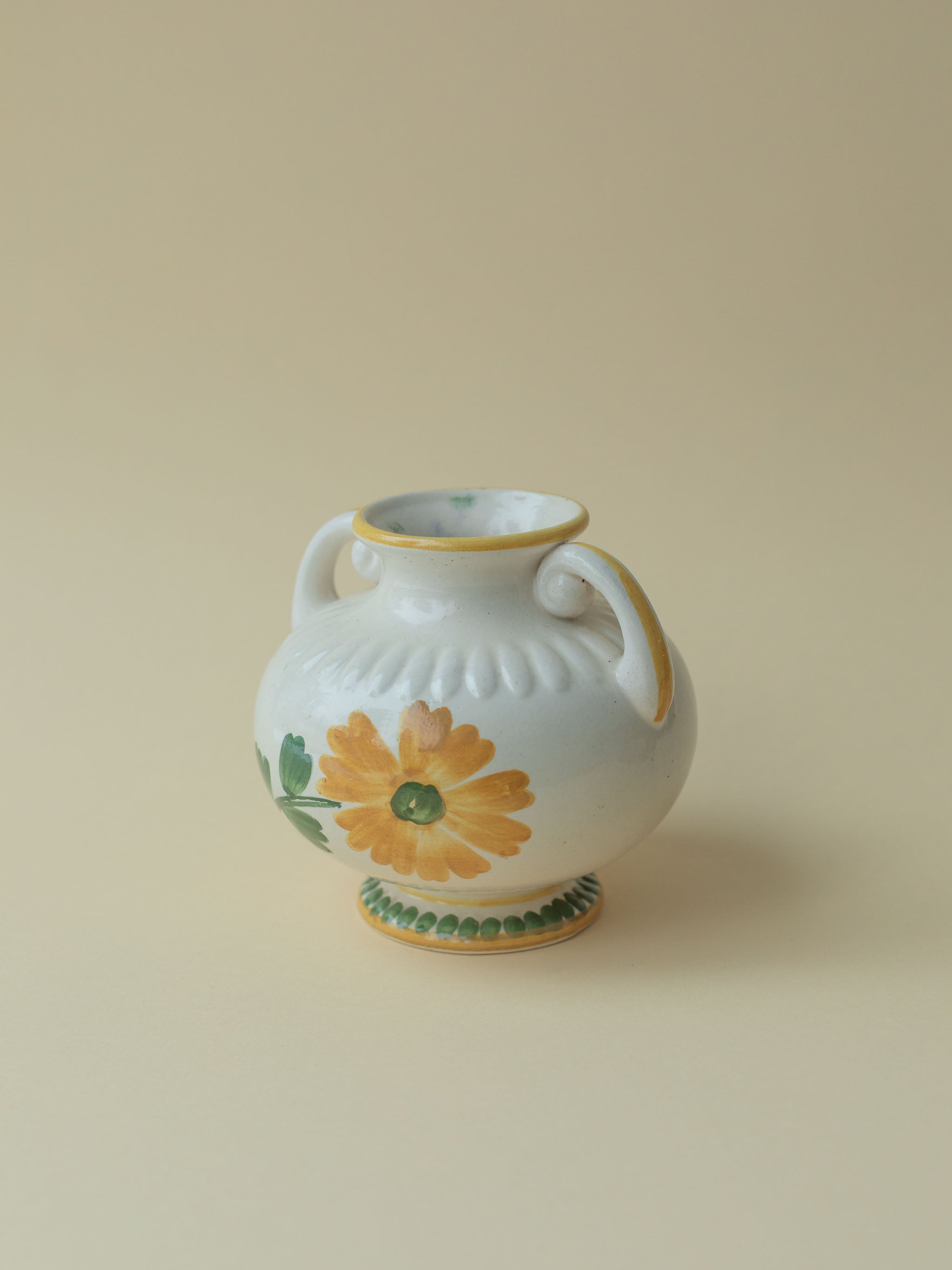A white vintage ceramic vase by Kupittaan Savi with a handpainted floral motif in green and yellow. Scandinavian design from Finland. A view from the front side angle.