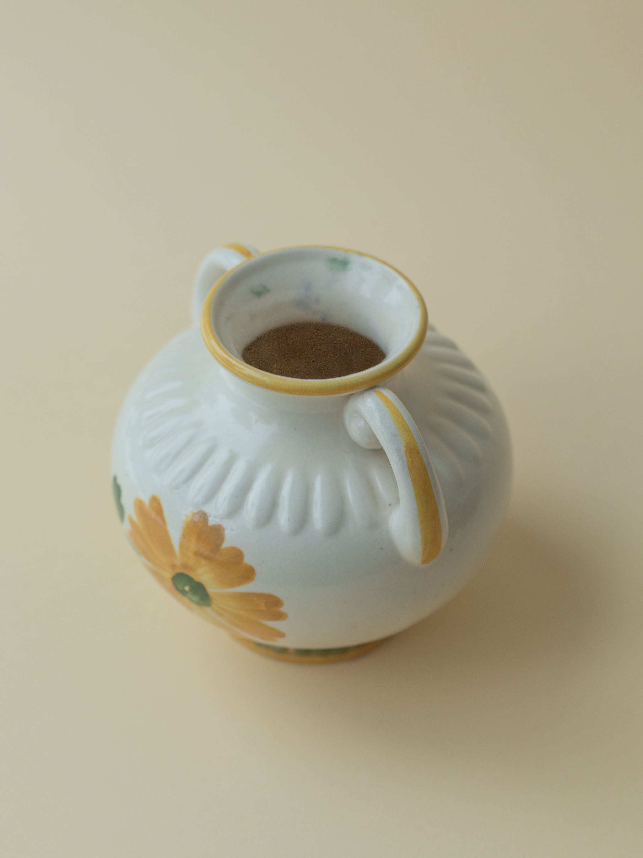 A white vintage ceramic vase by Kupittaan Savi with a handpainted floral motif in green and yellow. Scandinavian design from Finland. A view from the top, close up.