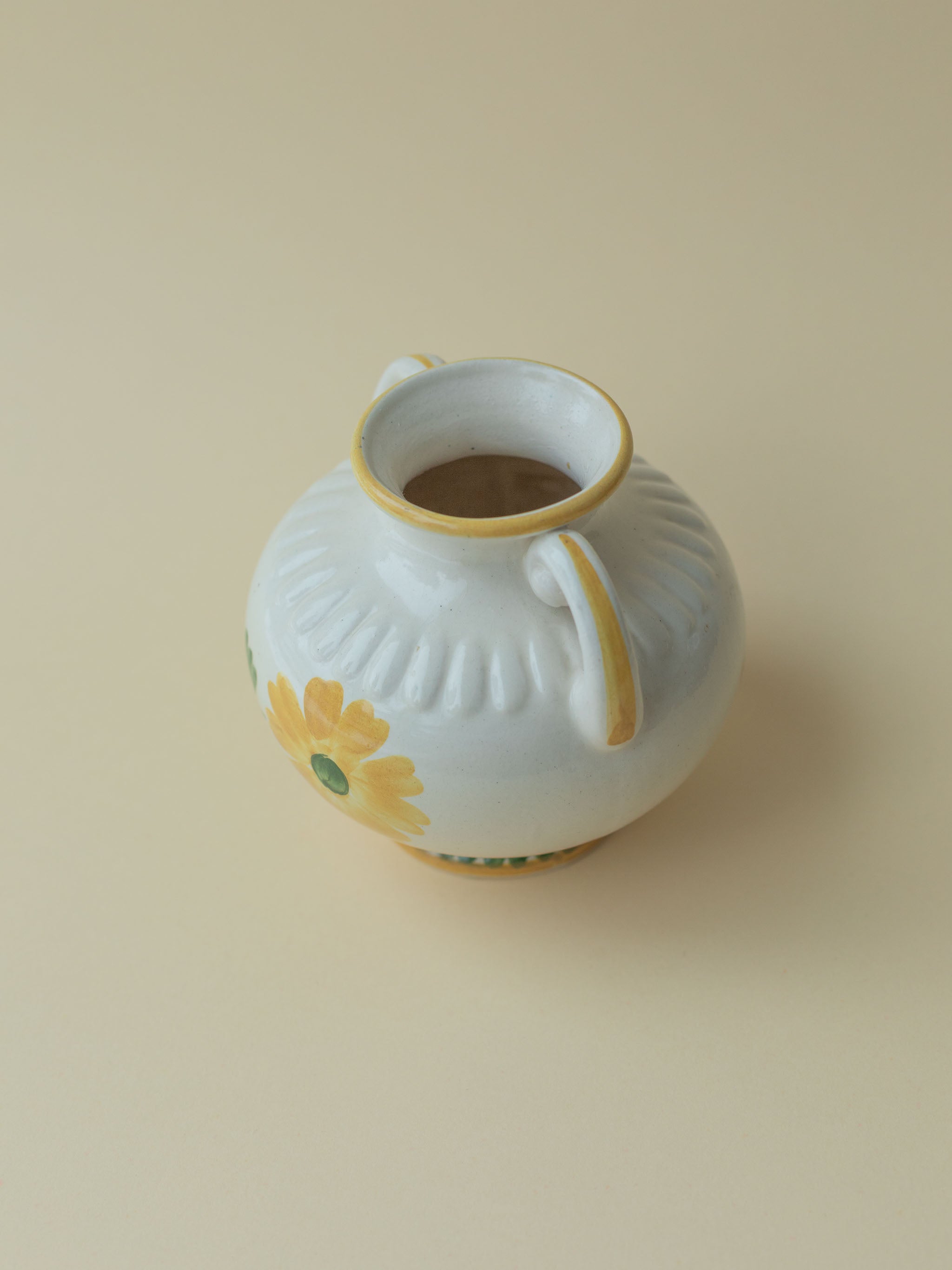 A white vintage ceramic vase by Kupittaan Savi with a handpainted floral motif in green and yellow. Scandinavian design from Finland. A view of the handle from the side.