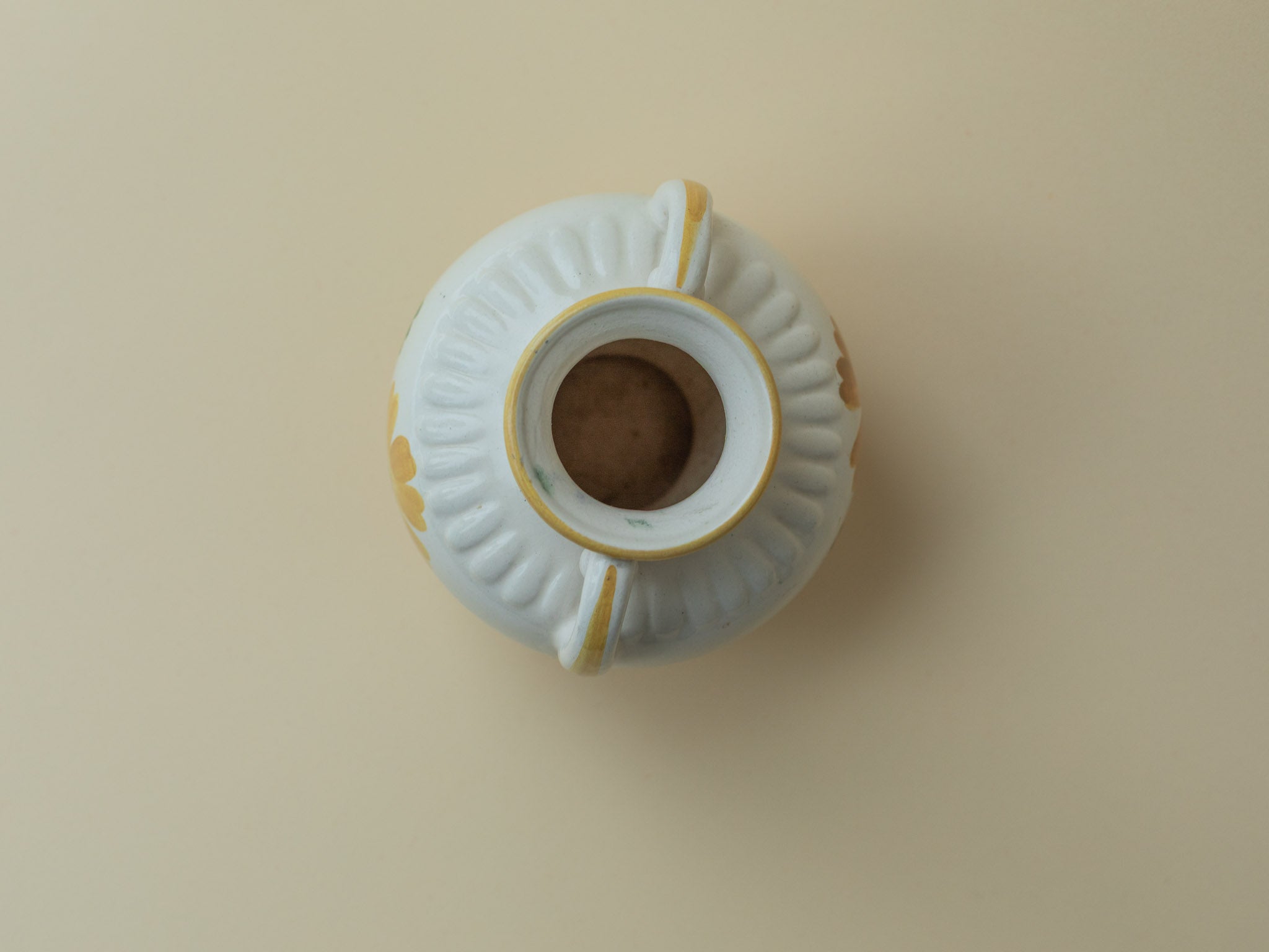 A white vintage ceramic vase by Kupittaan Savi with a handpainted floral motif in green and yellow. Scandinavian design from Finland. A view from the top, showing the inside of the vase.