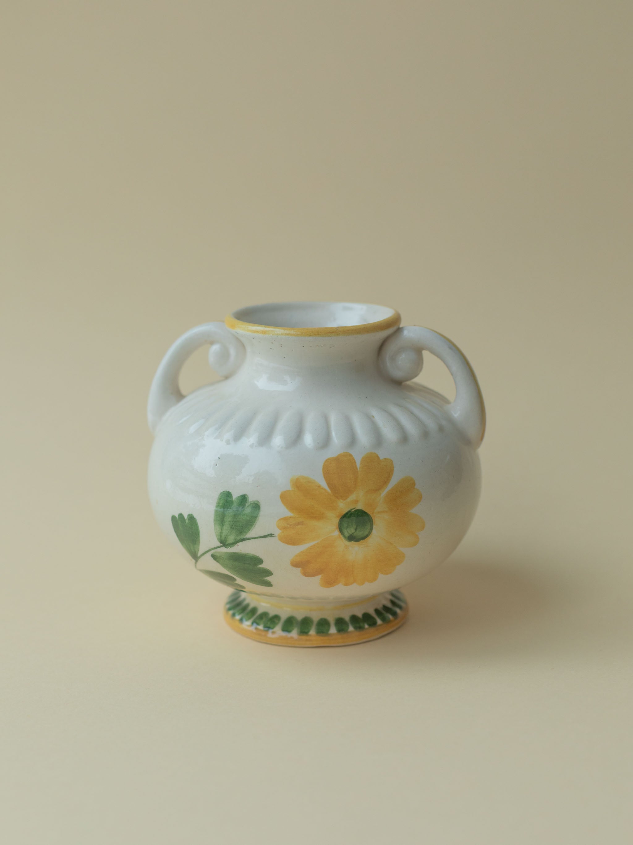 A white vintage ceramic vase by Kupittaan Savi with a handpainted floral motif in green and yellow. Scandinavian design from Finland. A view from the front.