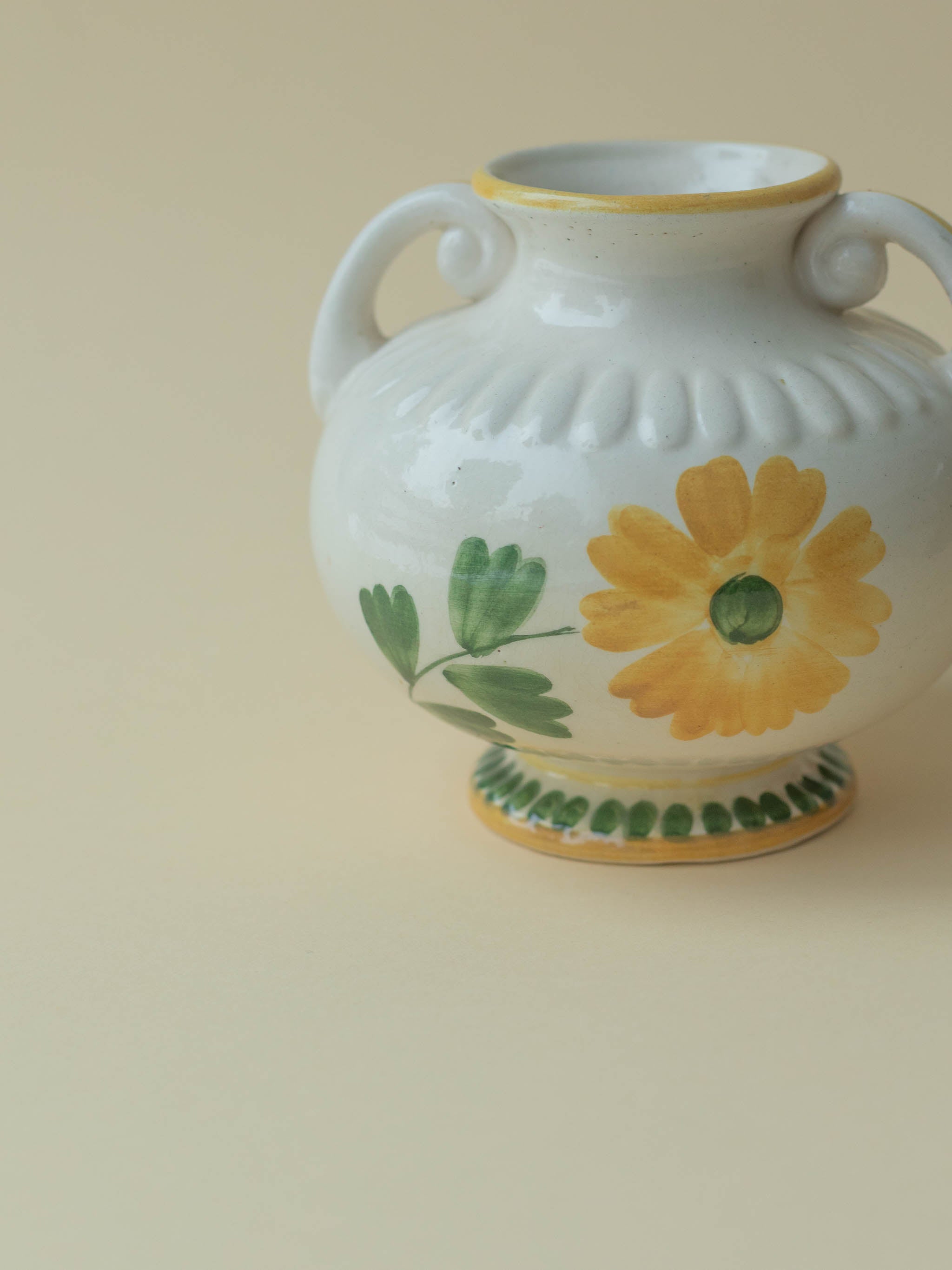 A white vintage ceramic vase by Kupittaan Savi with a handpainted floral motif in green and yellow. Signed at the bottom. Scandinavian design from Finland. A close up view from the front.